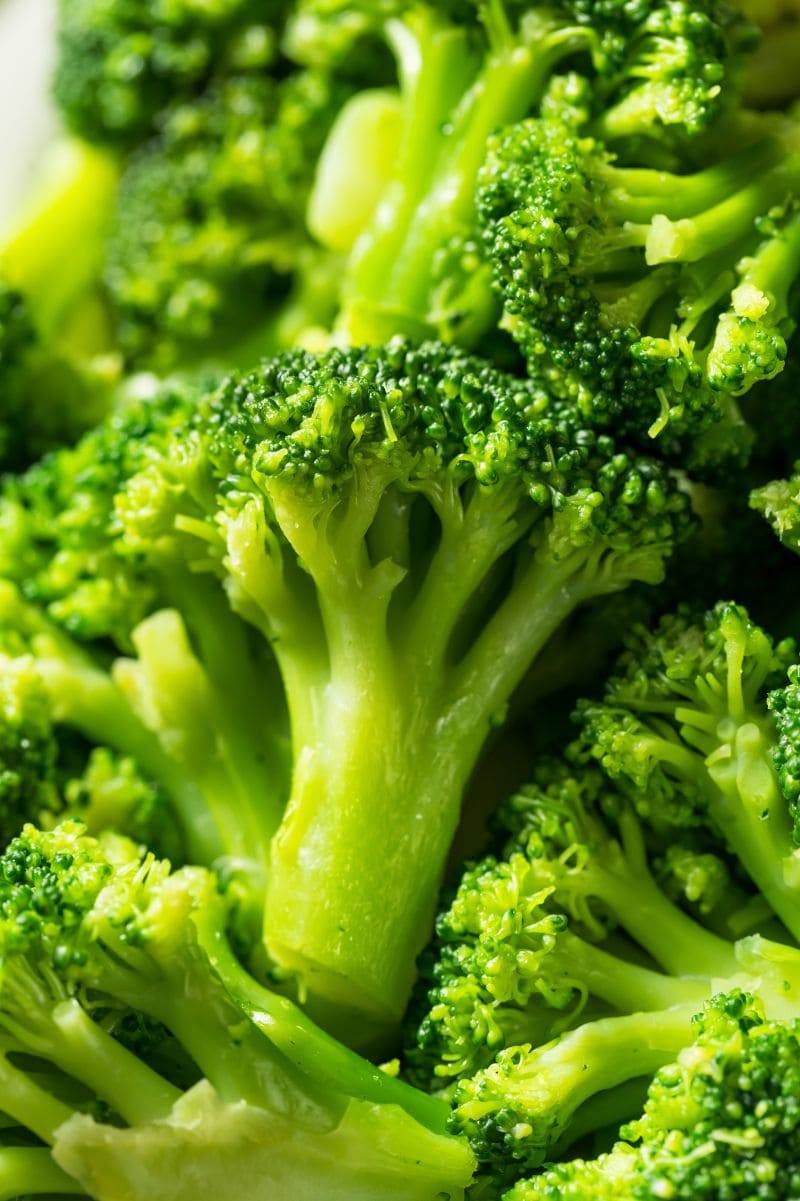 Tight view of a piece of bright green, tender broccoli in a pile of broccoli.