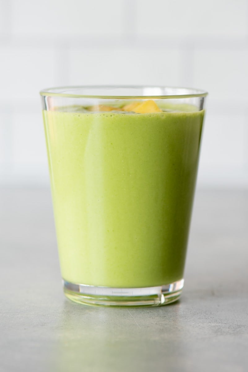 Side view of a pineapple green smoothie in a tall glass on a light background.