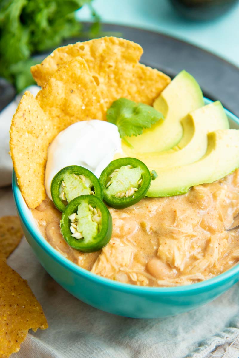 Serving bowl of chicken chili made in an Instant Pot garnished with fresh jalapeno slices, avocado slices, a dollop of sour cream, and corn tortilla chips.