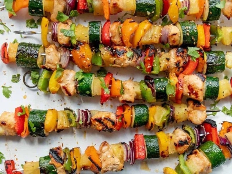 A white platter full of Grilled Hawaiian Chicken Kabobs on metal skewers