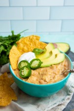 A teal bowl filled with Instant Pot white chili topped with sour cream, avocado, jalapeno, and corn tortilla chips.