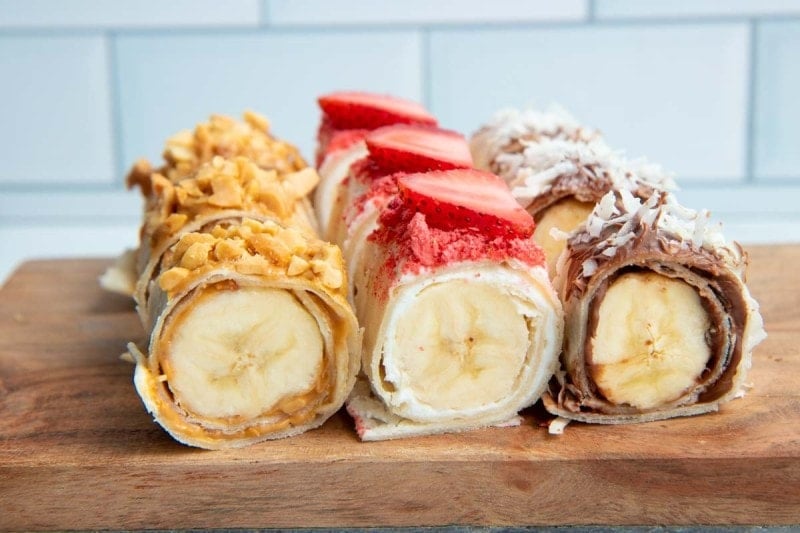 Close view of banana sushi flavors, including a peanut-topped peanut butter roll, a strawberry-topped strawberry roll, and a shredded coconut-topped nutella roll.