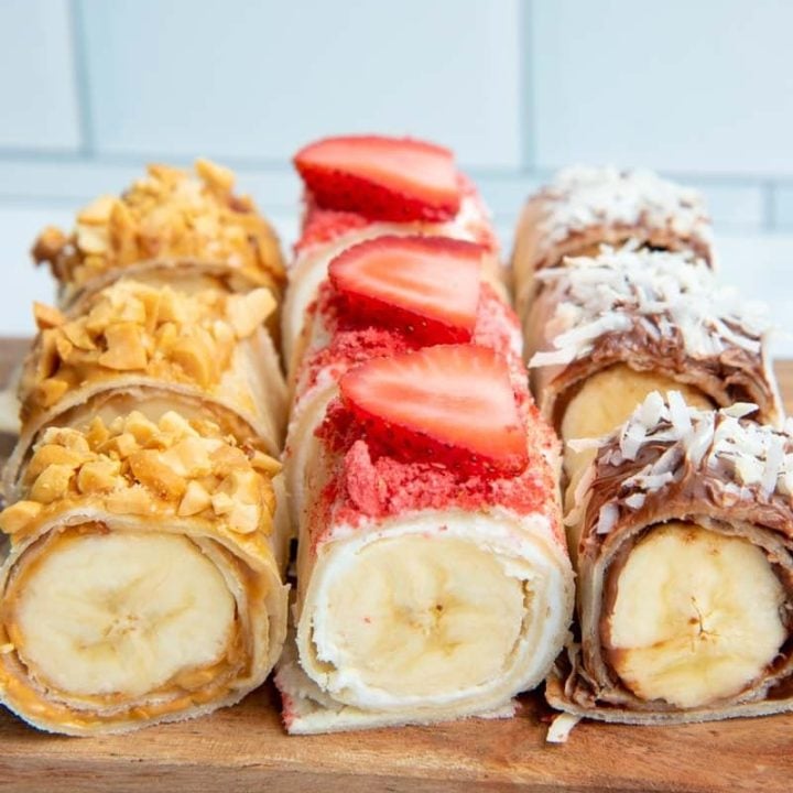 Close view of three flavors of banana sushi served on a wooden platter.