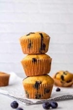 Three blueberry muffins stacked one atop the other on a parchment paper lined cooling rack.