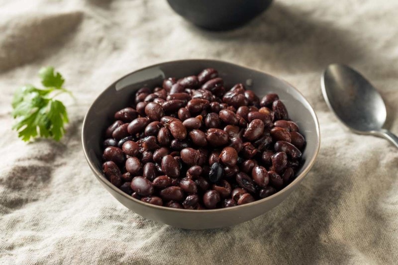 A gray bowl of instant pot cooked black beans with a spoon beside it on a linen tablecloth.