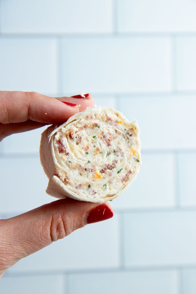 Close view of a hand holding up a chicken pinwheel showing the spiral of creamy filling inside.