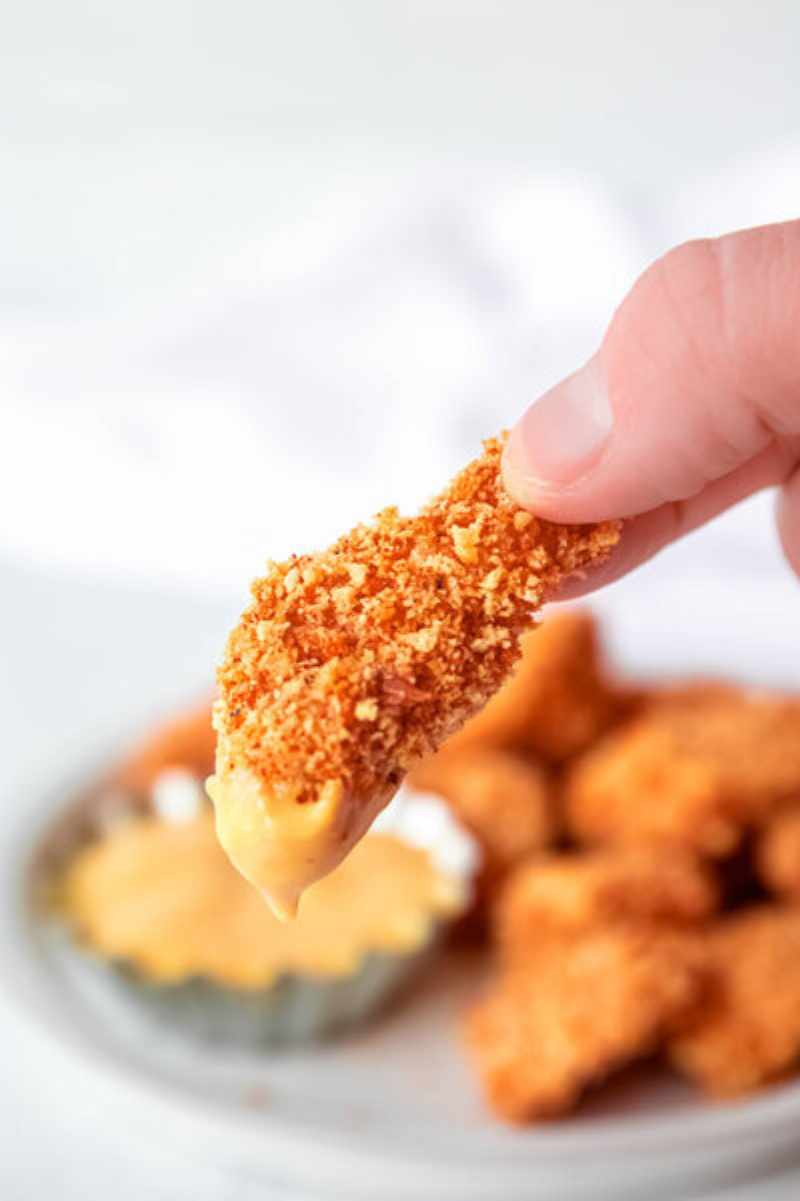 Two fingers hold up a crispy chicken nugget with creamy sauce on one end.