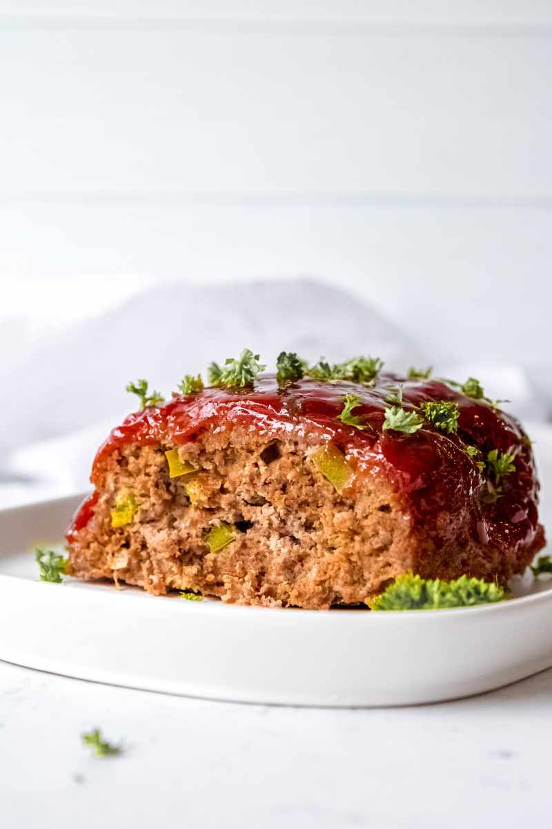 Finished meatloaf on a white serving platter with a slice removed to show the inside.