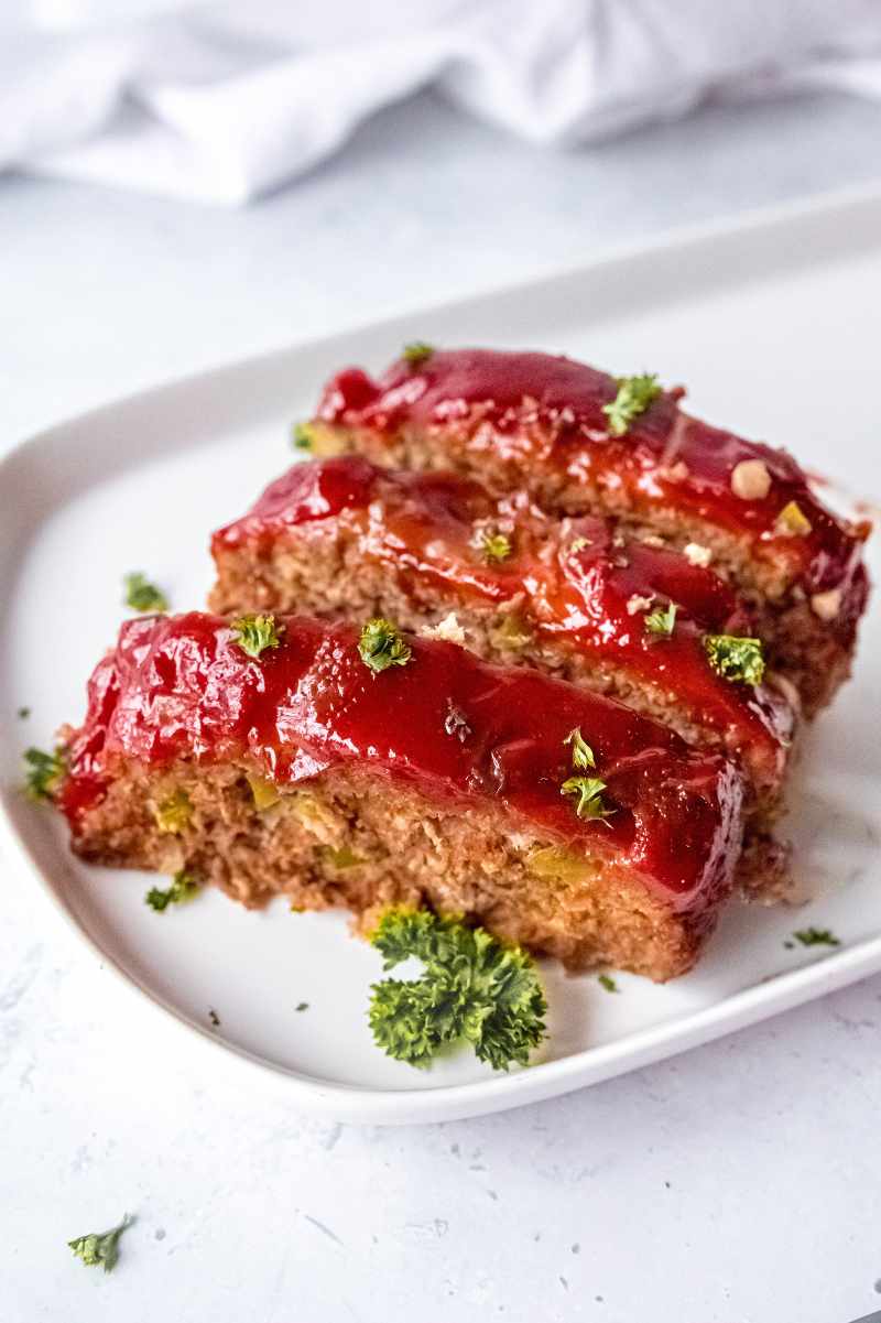 Three slices of meatloaf with a flavorful glaze on top garnished with fresh parsley.