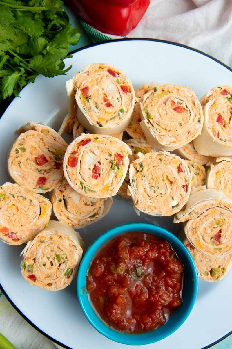Tight view of creamy pinwheel bites on a white platter with salsa for dipping.