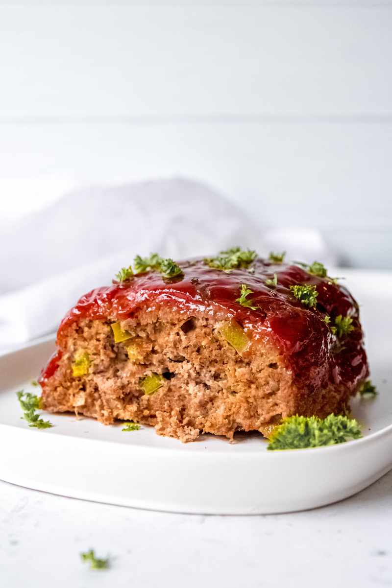 Classic meatloaf served on a white plate and garnished with fresh parsley.