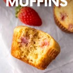 Close view of a strawberry muffin lying on its side with a bite taken out of it showing pockets of cooked pink fruit inside. A text overlay reads, "Strawberry Muffins."
