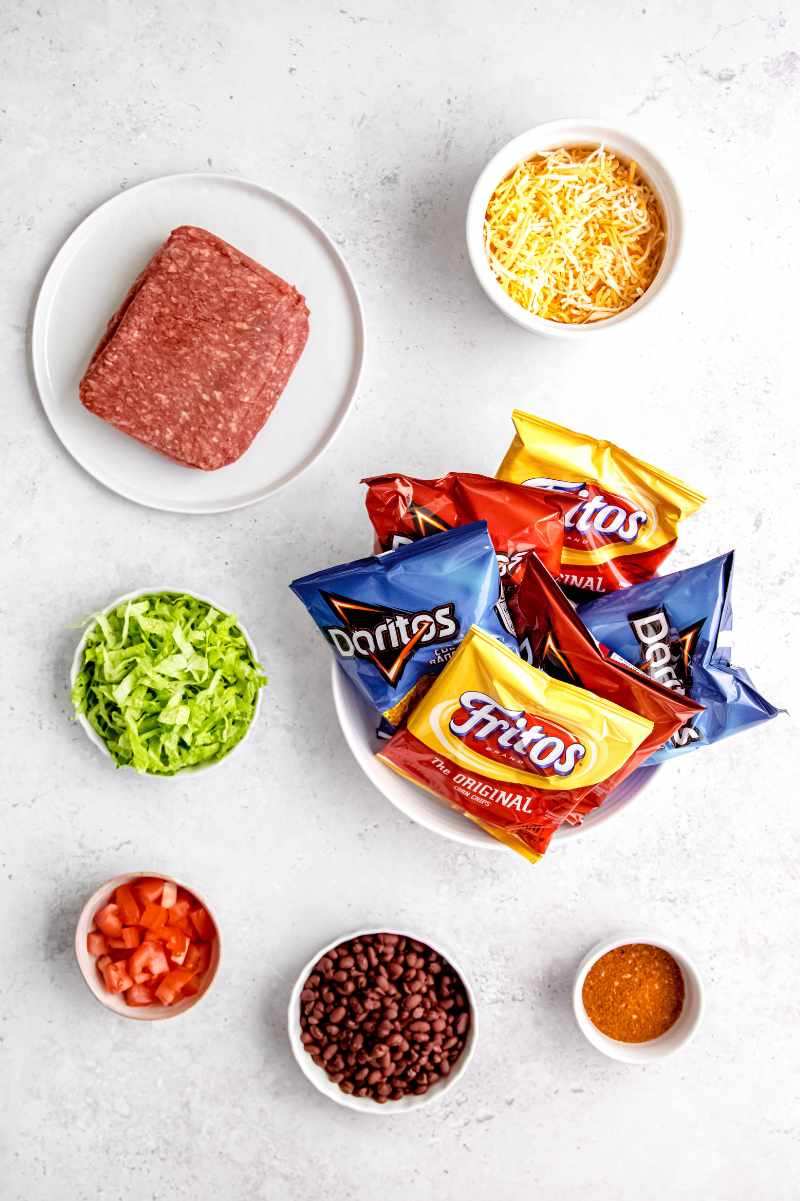 Overhead of all ingredients needed to make walking tacos, including ground beef, taco seasoning, taco fixings, and bags of chips.