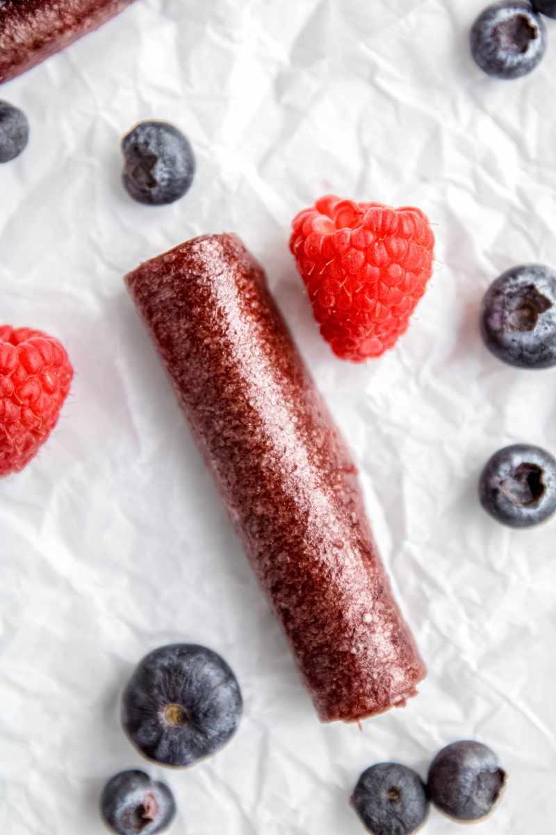 Close view of a berry roll-up surrounded by fresh raspberries and blueberries.