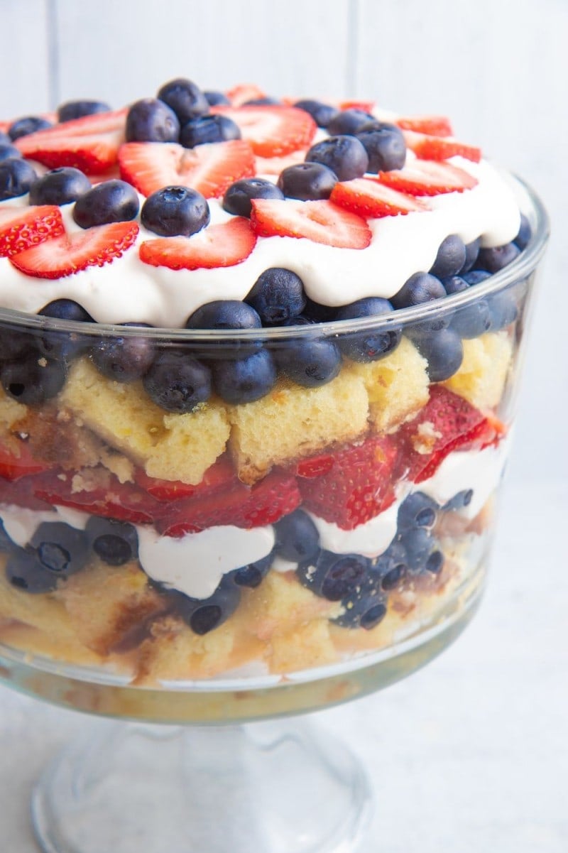 Close view of a summer berry trifle in a glass trifle dish showing distinct layers of berries, cream, and cake from top to bottom.