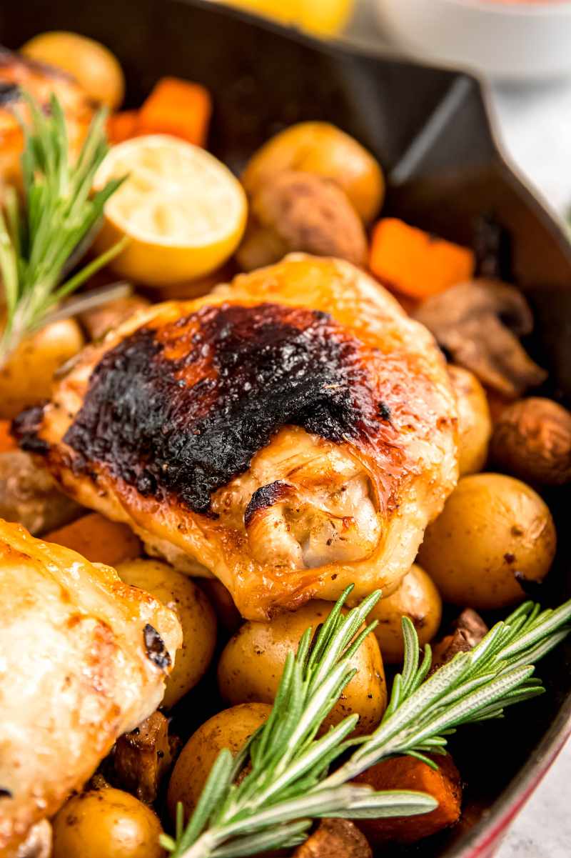 Tight view of lemon rosemary chicken thigh with dark, crispy skin on top of baby potatoes in a skillet.