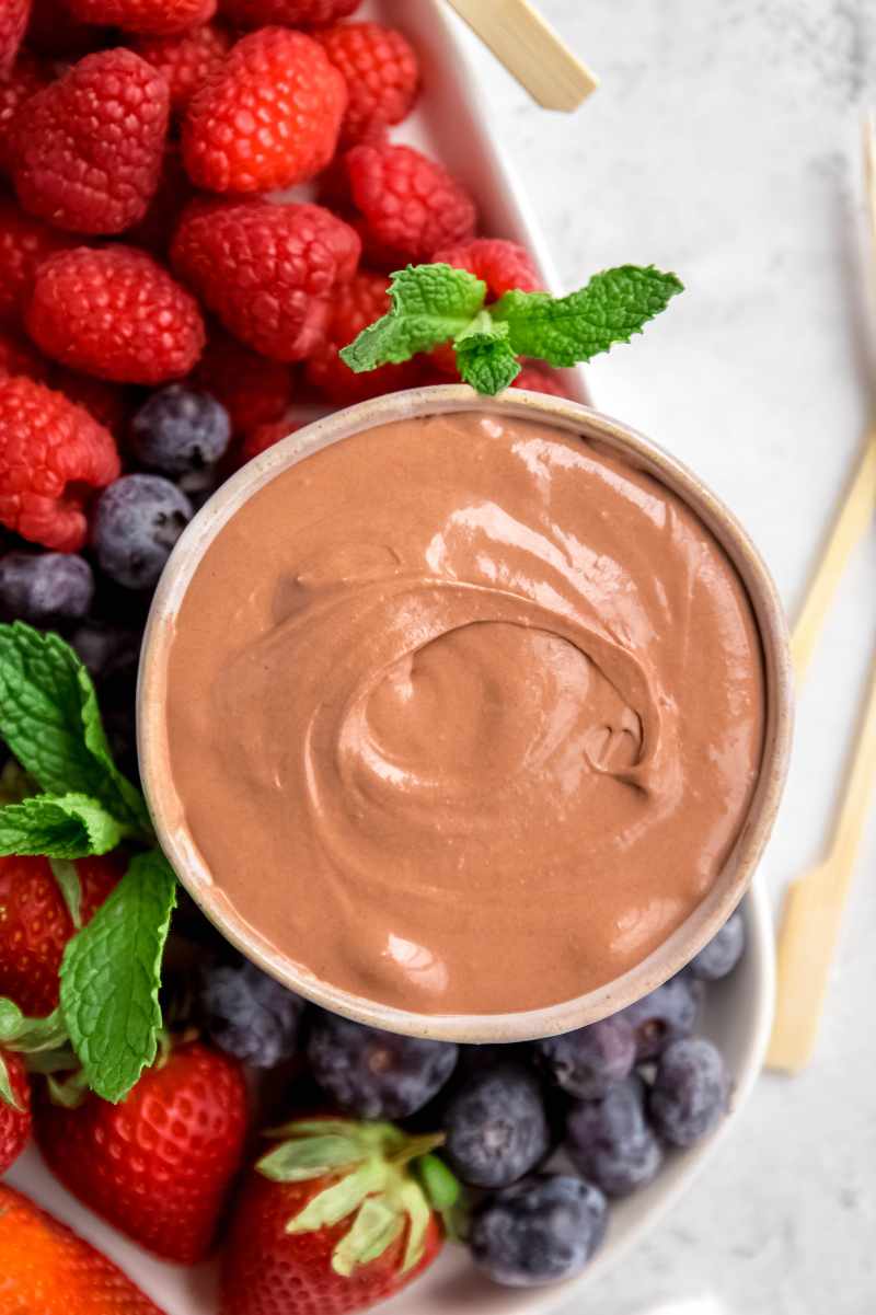 Top view of a bowl of chocolate marshmallow fruit dip surrounded by blueberries, raspberries, and strawberries.