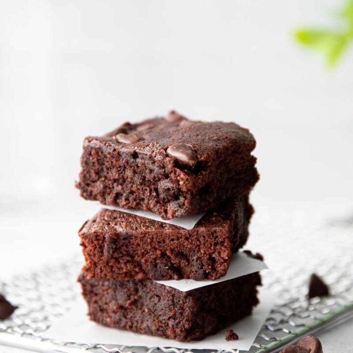 Three fudgy brownies stacked atop each other with parchment paper squares between them.