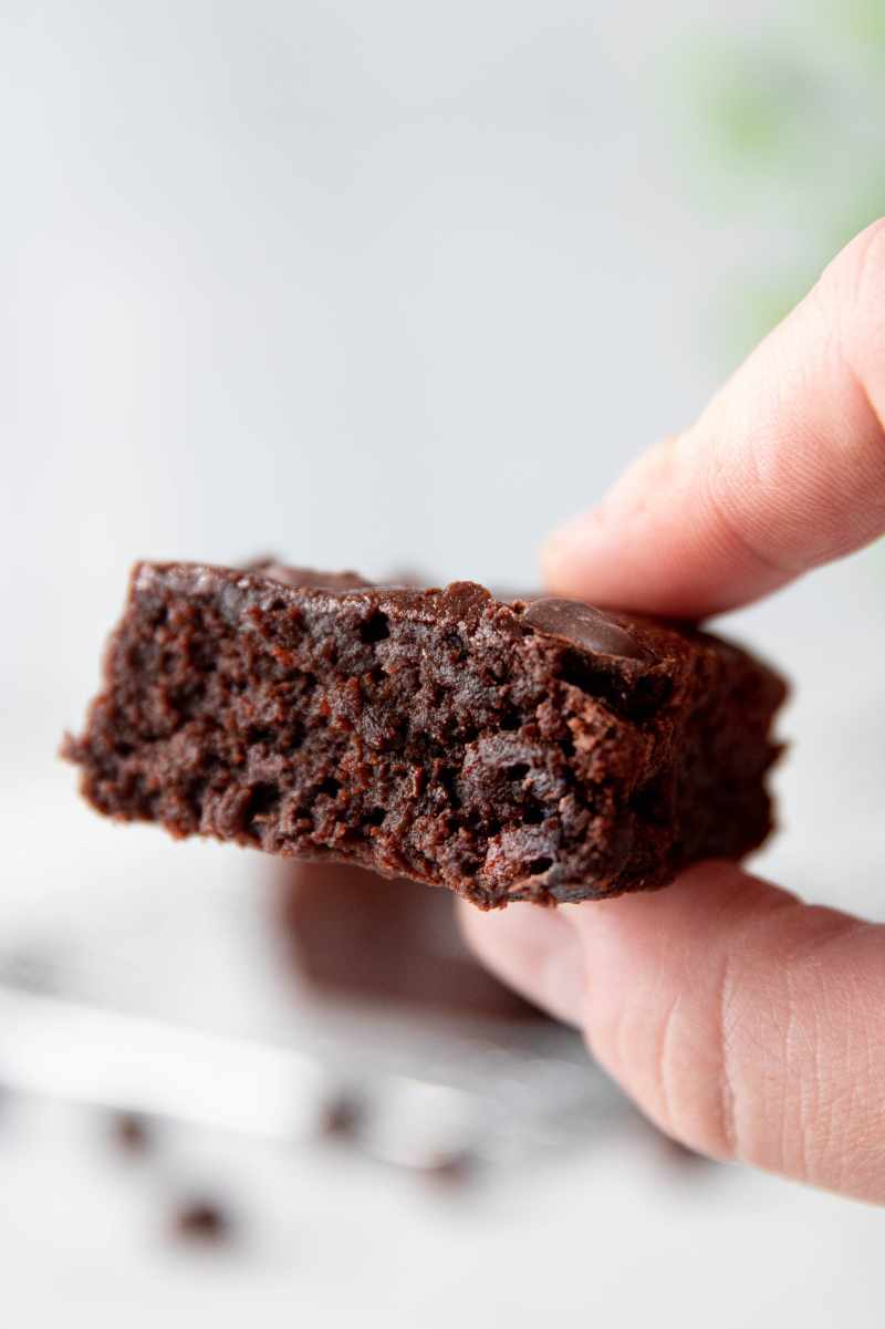 Two fingers hold up a gluten-free brownie made with almond flour showing the tender, fudgy inside.