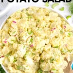 Top view of a large white bowl of potato salad with celery, red onion, and hard boiled eggs garnished with fresh dill. A text overlay reads, "Instant Pot Potato Salad."