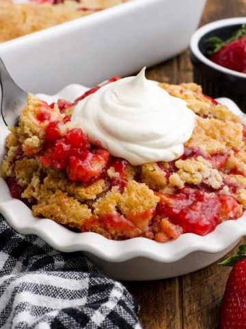 Close view of a fork scooping a bite of strawberry dump cake from a white bowl.