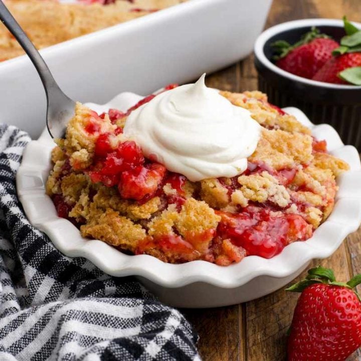 Close view of a fork scooping a bite of strawberry dump cake from a white bowl.