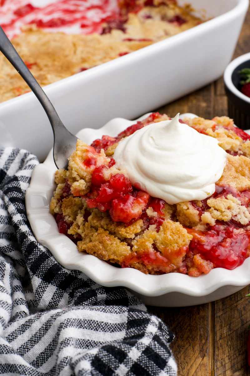 A fork digs into a bowl of easy strawberry dump cake.