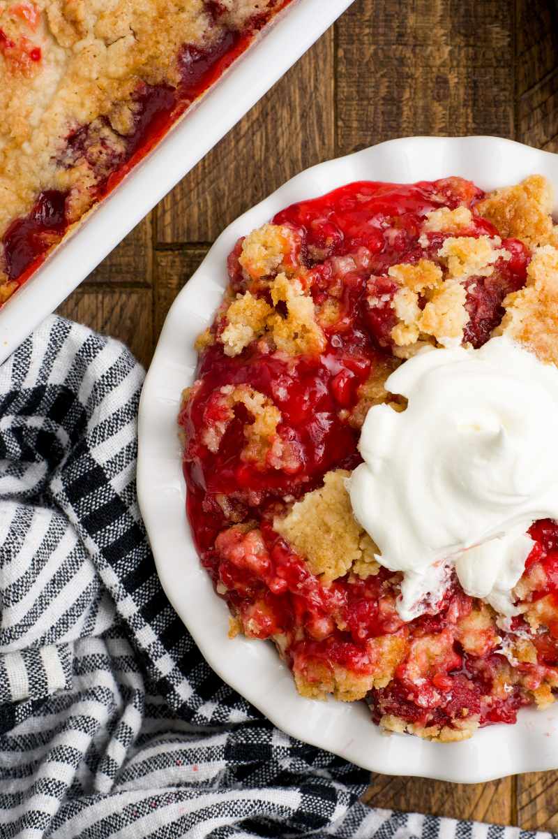 Top view of strawberry dump cake in a bowl topped with whipped cream.