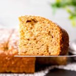 A metal spatula holds aloft a tall slice of banana cake dusted with powdered sugar.