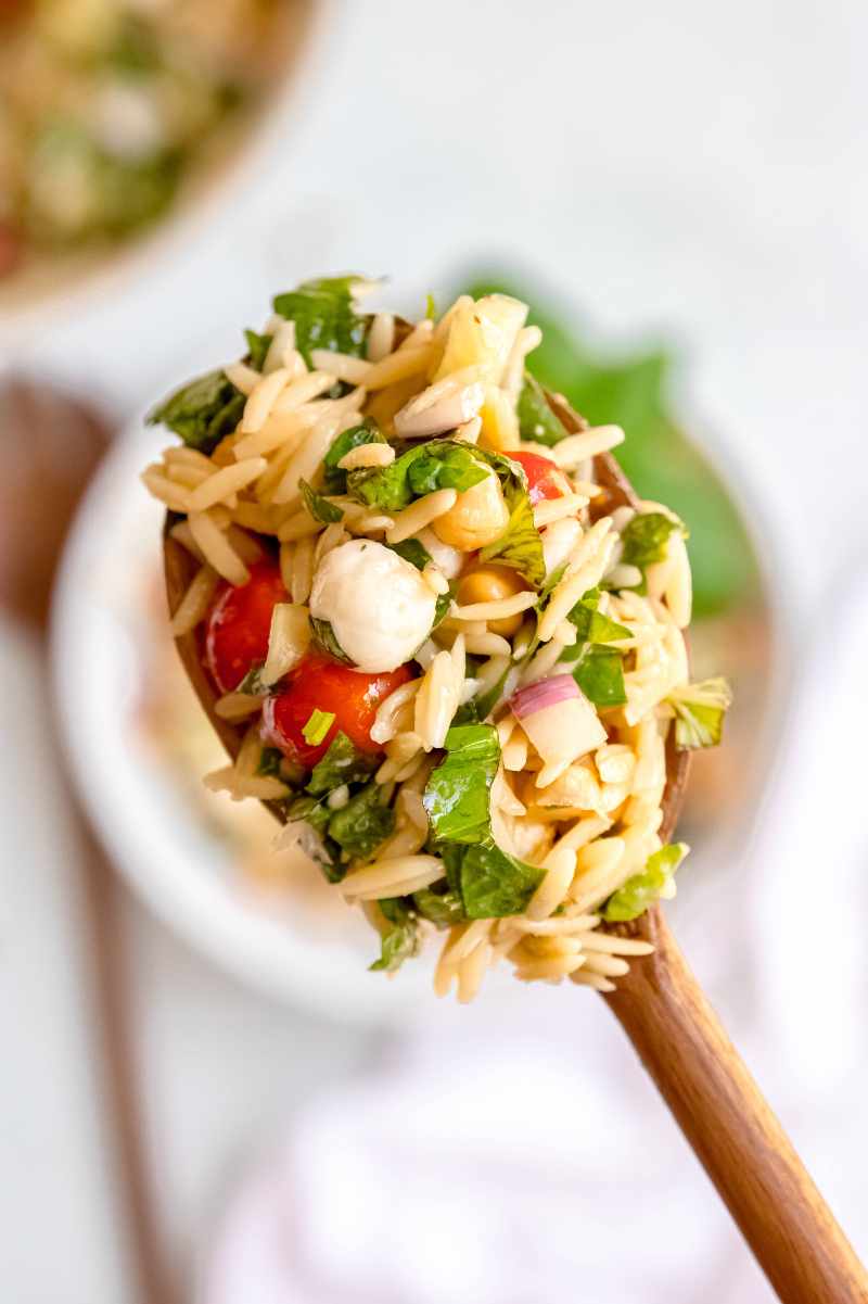 Close view of a scoop of orzo pasta salad on a wooden serving spoon.