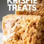 Close view of a peanut butter and marshmallow cereal square with three other cereal treats stacked behind it. A text overlay reads, "Peanut Butter Krispie Treats."