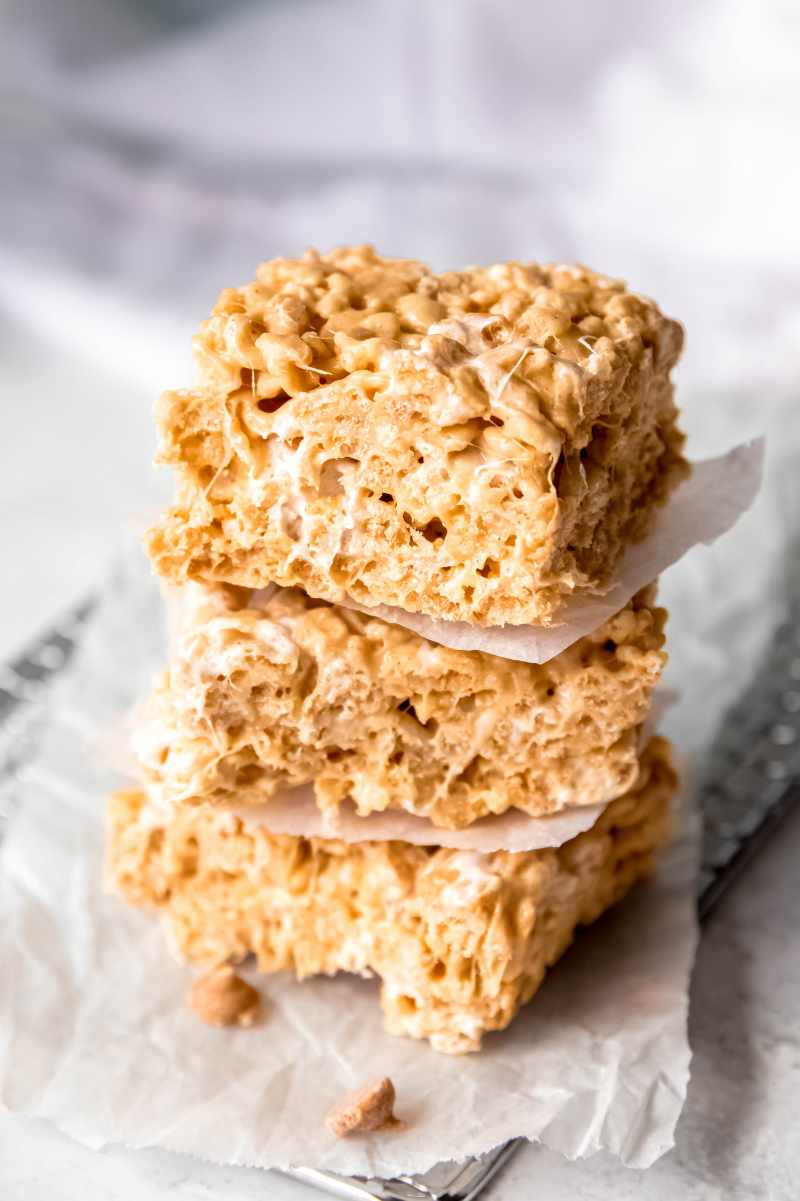 Close view of a stack of three cereal bars separated by parchment paper with peanut butter chips around them.