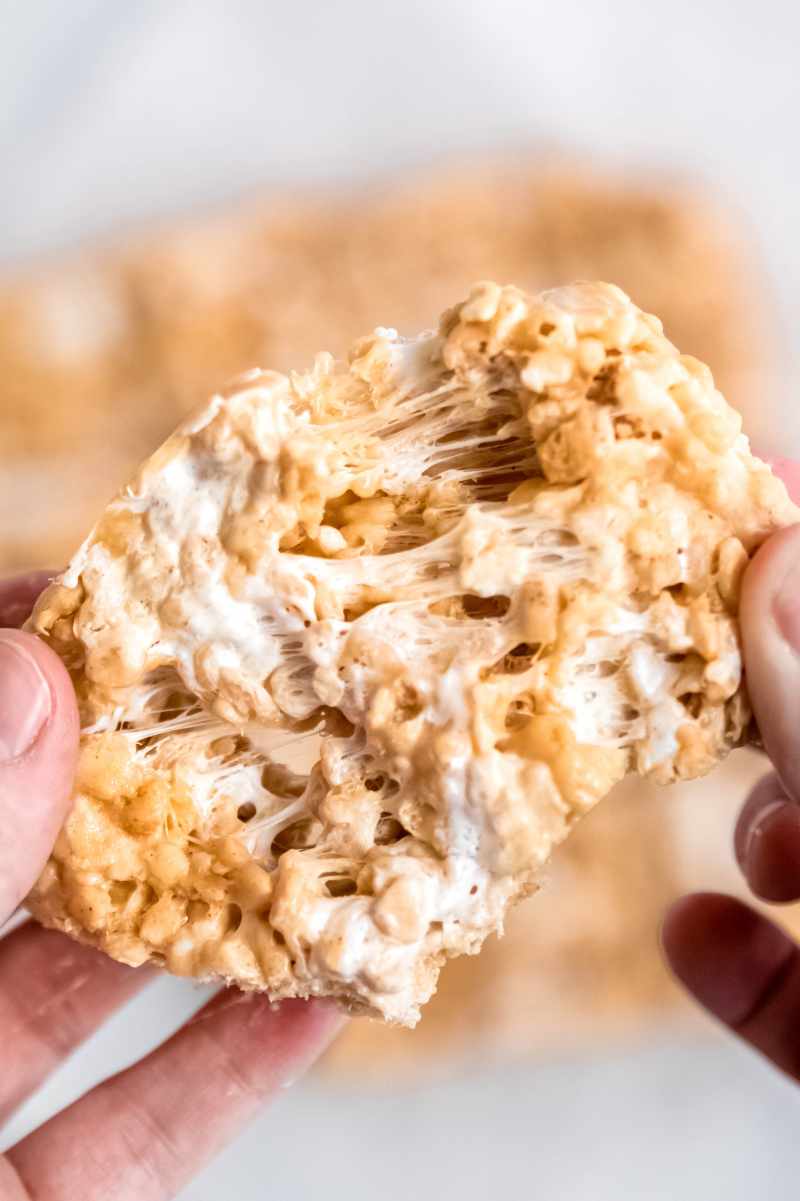 Two hands pull a homemade cereal bar showing gooey marshmallow strands.