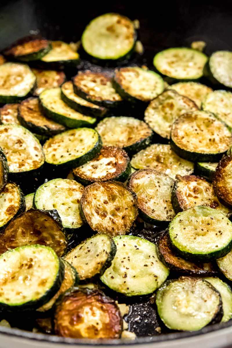 Slices of summer squash cooked in a cast iron skillet with garlic until tender and golden.