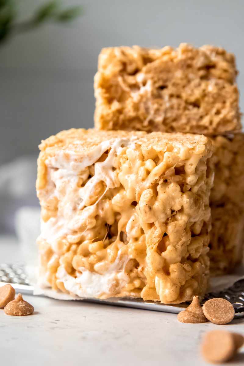 A peanut butter and marshmallow cereal square stands on a parchment paper lined cooling rack with three other cereal treats stacked behind it.