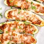 Close view of stuffed zucchini on a long white serving platter garnished with chopped fresh basil.
