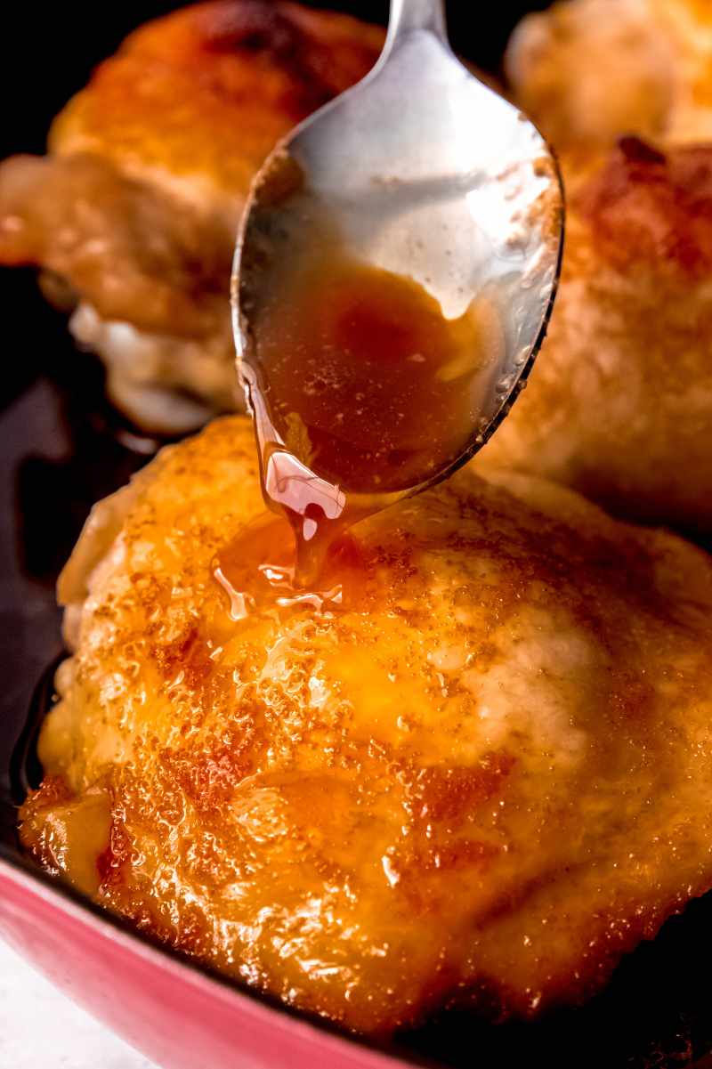 Close view of a spoon drizzling brown sugar sauce over perfectly baked dark meat thighs.