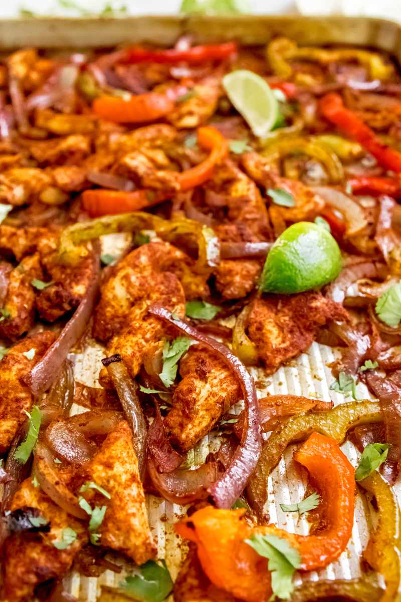 Chicken fajitas cooked on a baking sheet with seasoned meat and veggies garnished with cilantro and lime.