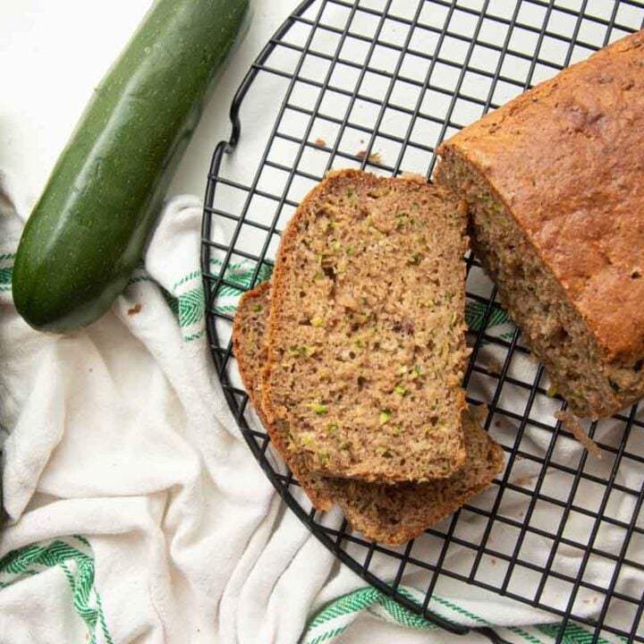 Overhead of a loaf of gluten-free zucchini bread on a cooling rack with two slices cut and stacked beside it.