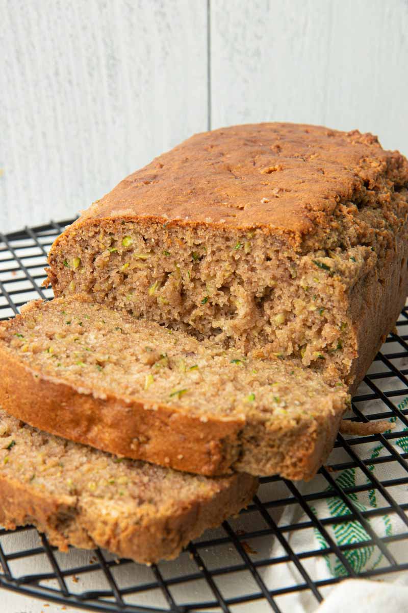 Close view of a loaf of gluten-free zucchini bread on a cooling rack with two slices cut showing the tender inside.