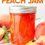 A jar of peach jam sits on a folded dishtowel, surrounded by fresh peaches. A text overlay reads, "Homemade Peach Jam."