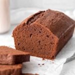 A sliced pound cake rests on a parchment paper lined cooling rack with a tall glass of milk in the background.