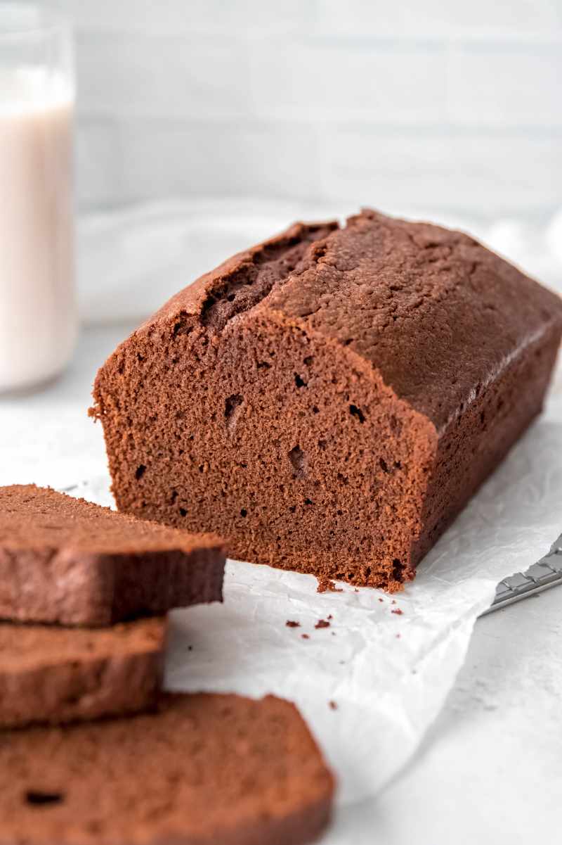 A sliced pound cake rests on a parchment paper lined cooling rack with a tall glass of milk in the background.