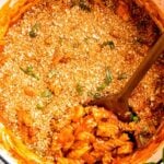 Overhead view of a wooden spoon scooping chicken parmesan pasta from a white enameled dutch oven.