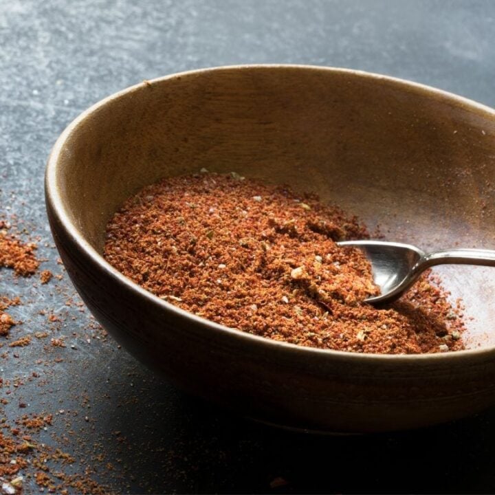 A spoon rests in a wooden bowl with homemade taco seasoning in it.