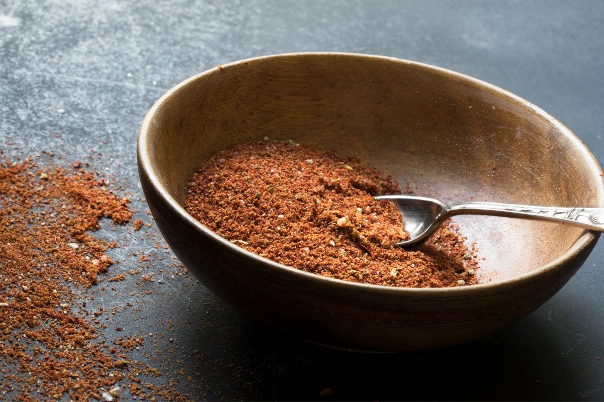 A spoon rests in a wooden bowl with homemade taco seasoning in it.
