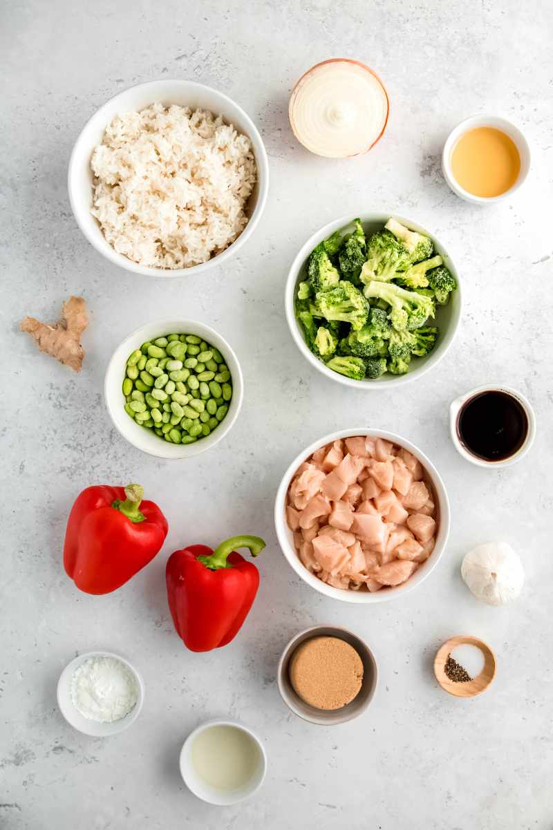 Overhead of all ingredients needed to make teriyaki bowls including rice, vegetables, brown sugar, and soy sauce.