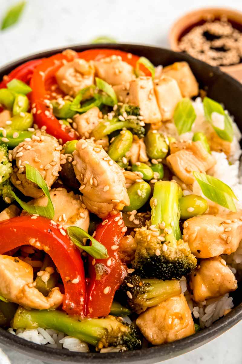 Tight view of teriyaki chicken and vegetables such as broccoli, bell peppers, and edamame served over rice.