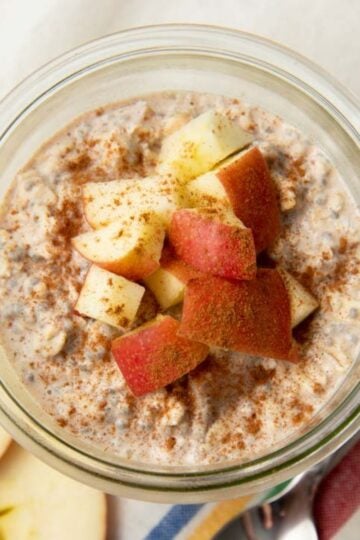 Apple cinnamon overnight oats in a glass jar sitting on a striped kitchen towel