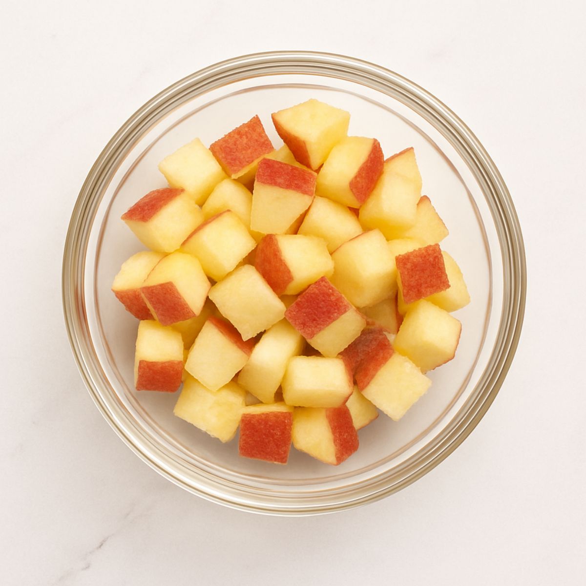 Apple chunks in a glass bowl on a white marble countertop